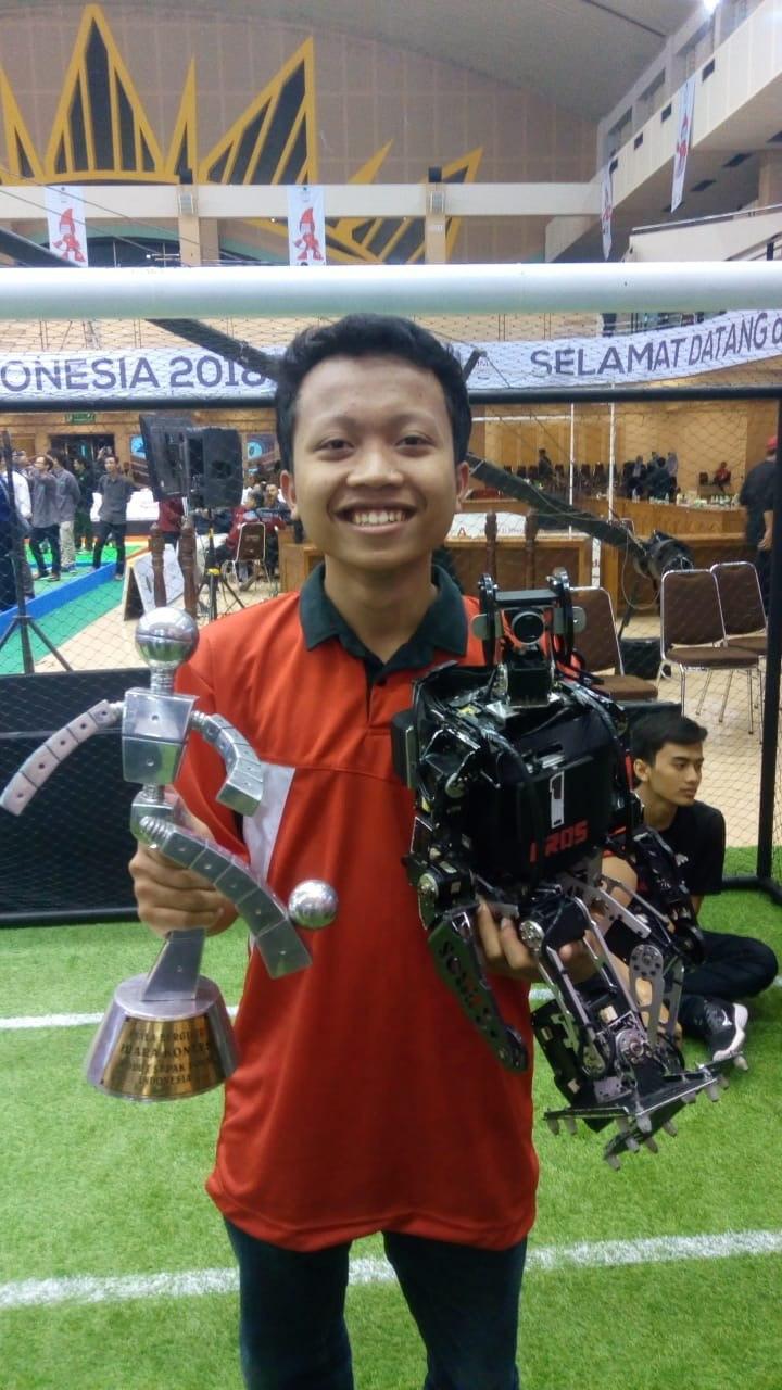Miftahul Anwar holding a humanoid robot at a competition